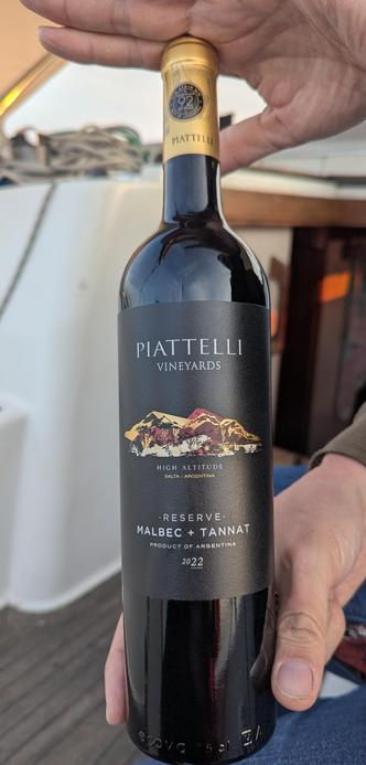 A dark glass wine bottle being held with two hands. Piatelli vineyard. Malbev + Tannat. 2022 Reserve vintage.