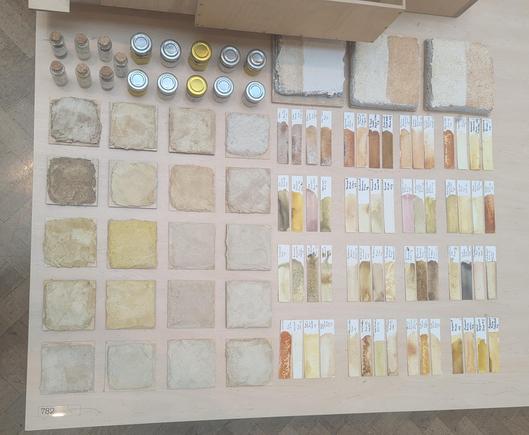 A geometrical display of small bottles, coated tiles and paper strip showing a muted range of colours ranging from blue/grey to brown and yellow.
