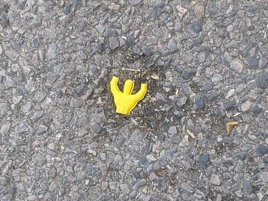 Bright yellow upper half of a plastic human figure with arms raised above head positioned into a small depression in the black/grey asphalt.