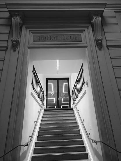 Stone carved sign Bibliotheque
above a well lit staircase ascending to glass doors.